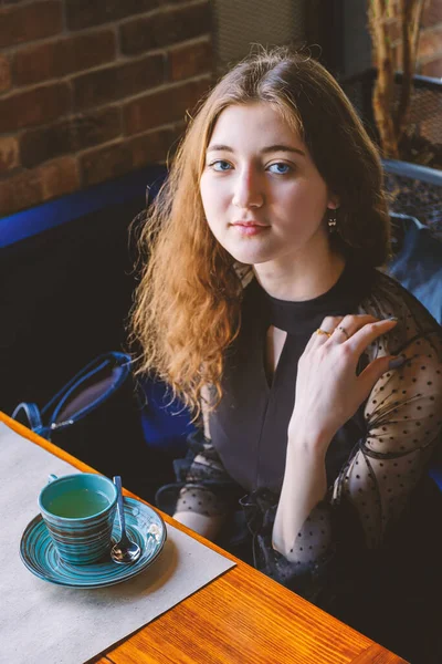 Deushka siedzi przy stole w ciepłej kawiarni przed nią stoi filiżanka gorącej herbaty, usunięta z góry. — Zdjęcie stockowe