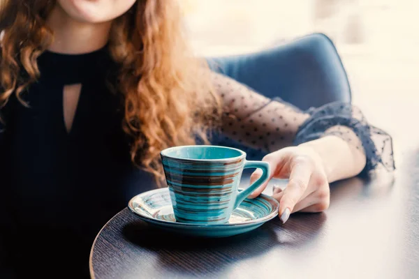 La fille aux cheveux roux s'assoit à une table dans un café et sa main touche une tasse en céramique verte dans le style japonais . — Photo