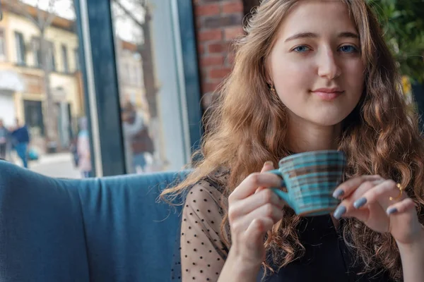 Een mooi rustig meisje houdt een kopje met een warm drankje en kijkt in de camera. — Stockfoto