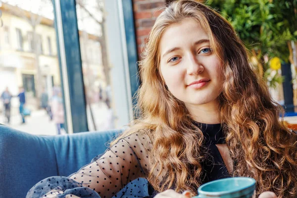Рыжая девушка с голубыми глазами сидит в кафе и смотрит в камеру — стоковое фото