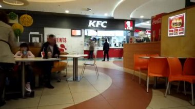 Astrakhan, Rusya, 27 Mart 2020: İnsanlar büyük bir alışveriş merkezinde arka plandaki KFC logosunda oturarak yemek yiyor