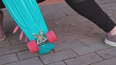 Sporcu kız bir bacağının üstüne çömelip kaykayla poz veriyor.