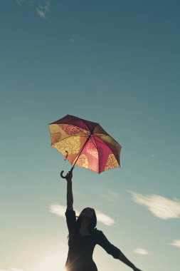 Kız silueti gökyüzüne doğru uzanıyor, şemsiyeyi tutan bir elle.