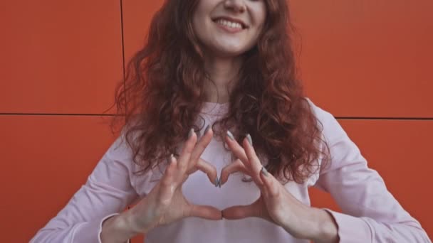 Het meisje maakte een hartvorm van haar vingers en trekt deze naar de camera. — Stockvideo