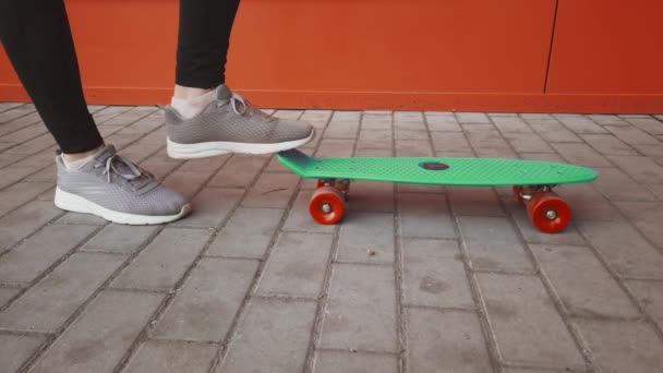 Meisje zet een stap naar het einde van een skateboard zodat hij op de achterwielen stapt, dan neemt ze een stap terug en de focus ligt op het skateboard op de stoep. — Stockvideo