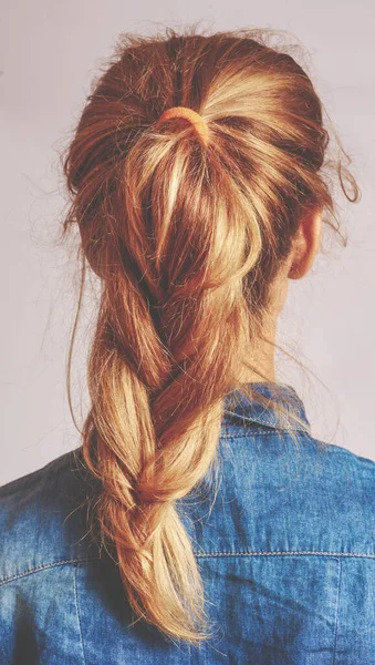 A visão traseira de uma jovem mulher com cabelo loiro tecida em uma trança desleixada e elegante de estilo francês . — Fotografia de Stock