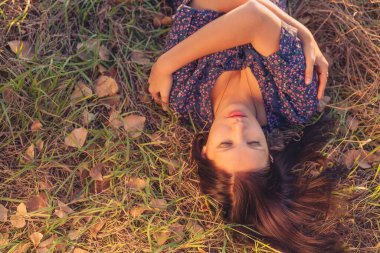 Genç kadın sonbaharda şişmiş çimenlerde uzanmış açık hava portresi.