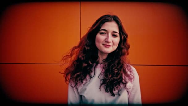 Giovane ragazza con i capelli ricci che sta contro un muro rosso e guarda nella fotocamera sorridente, grana forte, colore retrò e vignetta dura — Video Stock