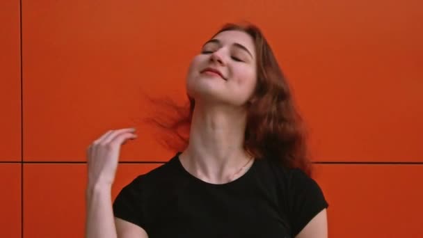 Una chica con cabello castaño posa contra una pared sacudiendo su cabello — Vídeo de stock