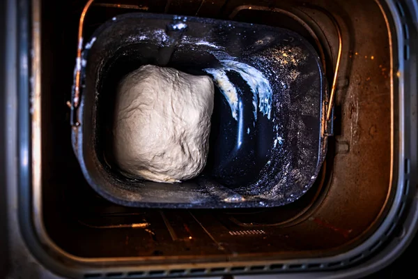 Teig in der Brotpfanne des Brotbäckers zu Hause. Nicht angehobener Teig, der sich auf das Backen in der schicken Brotbackmaschine vorbereitet. Ansicht von oben. — Stockfoto