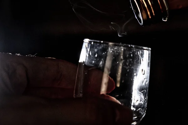 Een man houdt een glas vast waarop de hals van de fles wordt overzien en er een lichte waas uit rolt. — Stockfoto