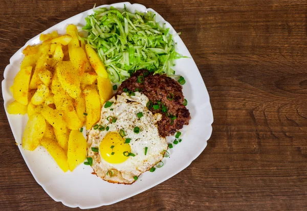 Bife grelhado Bife com ovo frito, salada de legumes e batata em um prato branco na mesa de madeira — Fotografia de Stock