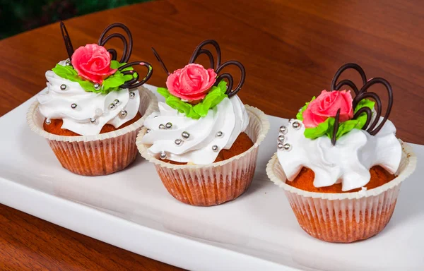 Νόστιμα κόκκινο βελούδο cupcakes διακοσμημένα με ροζ τριαντάφυλλο σε φόντο ξύλινη — Φωτογραφία Αρχείου