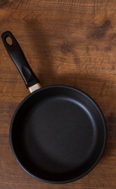 Kahverengi ahşap masa arka plan üzerine boş siyah kızartma tavası. kopya alanı ile. Üstten Görünüm.