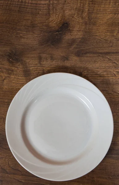Leerer weißer Teller auf dem braunen Holztischhintergrund. mit Kopierraum. Ansicht von oben. — Stockfoto