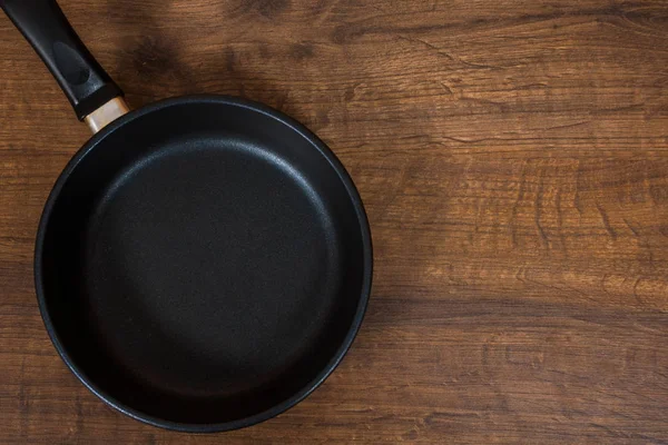 Black Frying Pan kosong pada latar belakang meja kayu coklat. dengan ruang fotokopi. tampilan atas . — Stok Foto