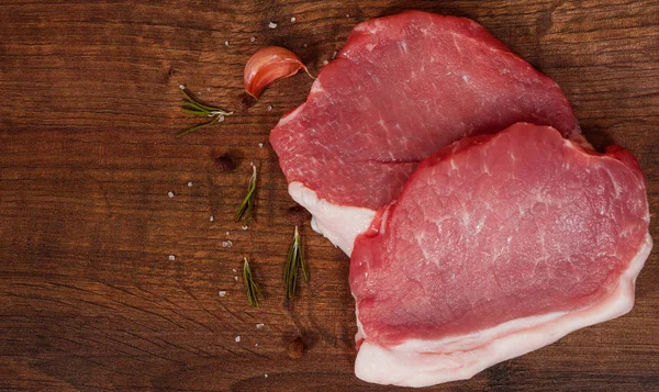 çiğ domuz eti biftek ve sarımsak, biber kahverengi ahşap masa arka plan üzerinde. rustik mutfak masasında kopya alanı ile. Üstten Görünüm.