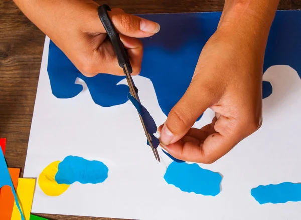 Un enfant découpe du papier. Feuilles de papier coloré. L'art des enfants. Concept d'artisanat. Fait main. sur table en bois vue du dessus . — Photo