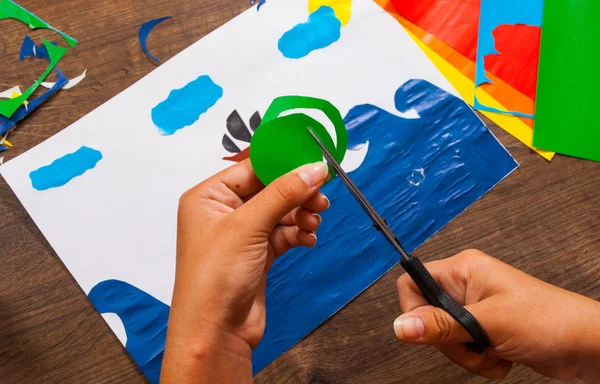 Kind snijdt papier. Vellen gekleurd papier. Kunst van de kinderen. Ambachten concept. Handgemaakte. op houten tafel bovenaanzicht. — Stockfoto