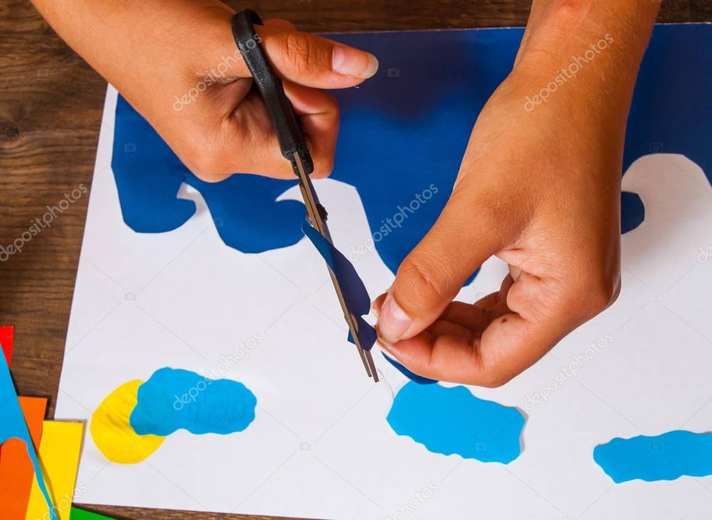 Child cuts out of paper. Sheets of colored paper. Kids art. Crafts concept. Handmade. on wooden table top view.