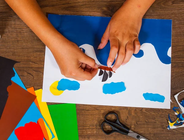 Kind lijmen van papier. Vellen gekleurd papier. Kunst van de kinderen. Ambachten concept. Handgemaakte. op houten tafel bovenaanzicht. — Stockfoto