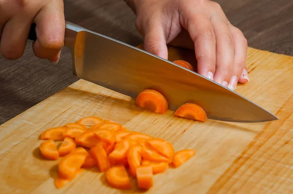 Шеф-повар рубит морковку на деревянной доске — стоковое фото