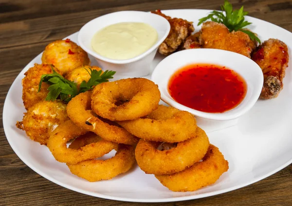 Conjunto de aperitivos. bolas salgadas, asas de frango, anéis de cebola, molho em um fundo de madeira . — Fotografia de Stock