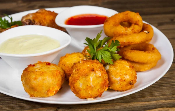 meze kümesi. tuzlu topları, tavuk kanatları, soğan halkaları, ahşap bir arka plan üzerine sos. 