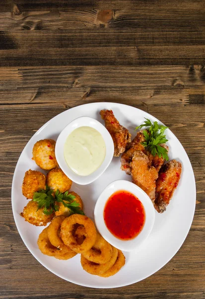 meze kümesi. tuzlu topları, tavuk kanatları, soğan halkaları, ahşap bir arka plan üzerine sos. kopya alanı ile. Üstten Görünüm