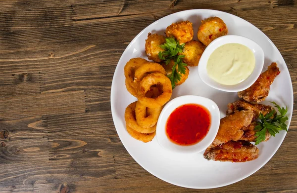 Conjunto de aperitivos. bolas salgadas, asas de frango, anéis de cebola, molho em um fundo de madeira. com espaço de cópia. vista superior — Fotografia de Stock