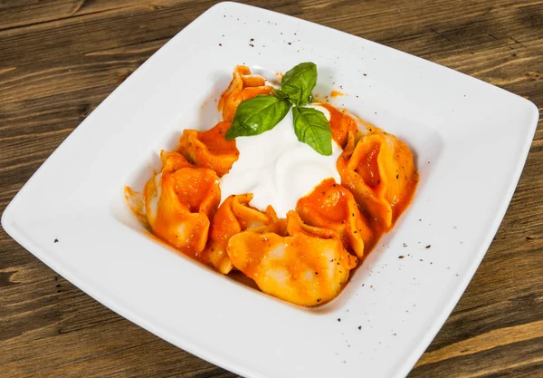 Ravioli topped with tomato sauce,with cheese and the fresh basil on white plate. on a wooden background. — Stock Photo, Image