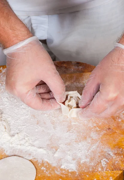 chef hands in process of making home-made dumplings, ravioli or pelmeni