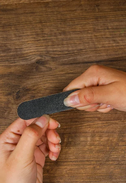 Manos sobre la mesa con manicura. El aserrado hace la forma de la uña. sobre un fondo de madera. con espacio para copias. vista superior — Foto de Stock