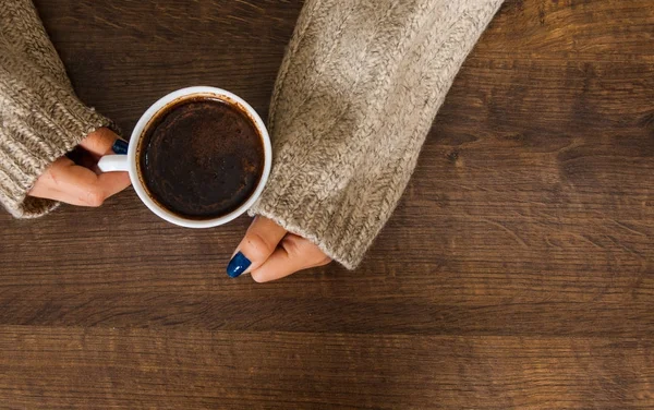 Woman's hands in sweater holding cup of coffee on the wooden table. with copy space. top view — Stock Photo, Image