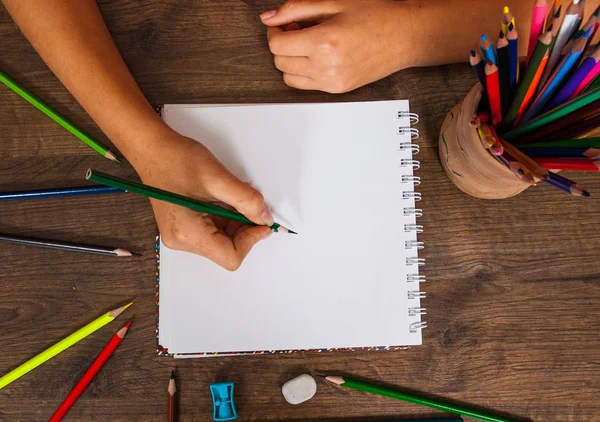 Meisje handtekening, blanco papier en kleurrijke potloden op houten tafel — Stockfoto