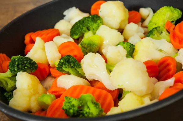 Mixed vegetables. cauliflower, broccoli and carrots in an iron pan on a wooden background.