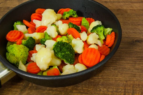 Mixed vegetables. cauliflower, broccoli and carrots in an iron pan on a wooden background.