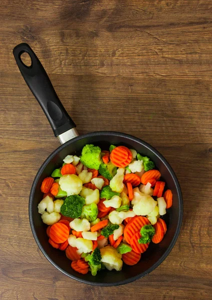 Vegyes zöldség. karfiol, brokkoli és a sárgarépa egy vas serpenyőbe egy fából készült háttér. — Stock Fotó