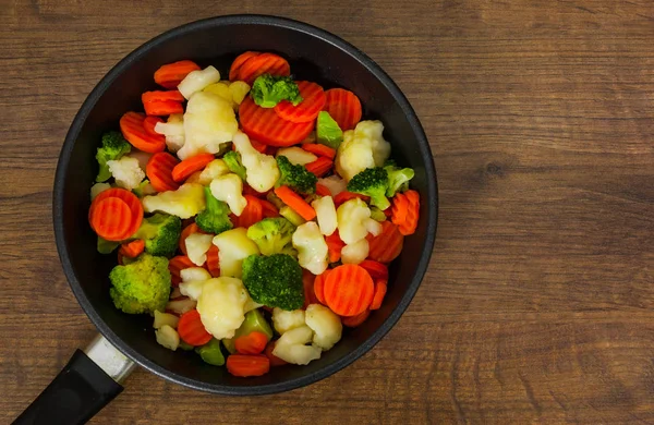 Mixed vegetables. cauliflower, broccoli and carrots in an iron pan on a wooden background.