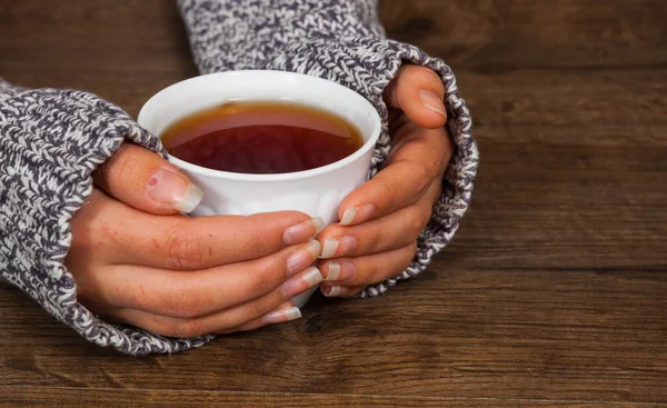 Manos de mujer sosteniendo taza de bebida de té caliente en la mesa de madera. con espacio de copia . — Foto de Stock