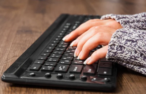 Woman hand typing on black keyboard on a wooden background.