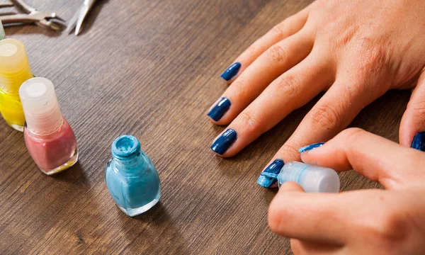 Manicura. Primer plano de una mujer pintándose las uñas con esmalte de uñas sobre un fondo de madera . — Foto de Stock