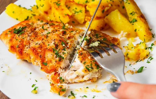 Mulher mão segurando garfo e faca com peito de frango grelhado com batata em uma placa em um fundo de madeira — Fotografia de Stock