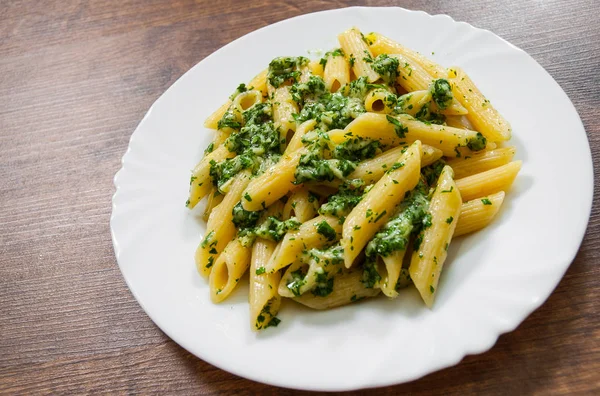 Penne pasta with pesto sauce in plate on a wooden background. — Stock Photo, Image