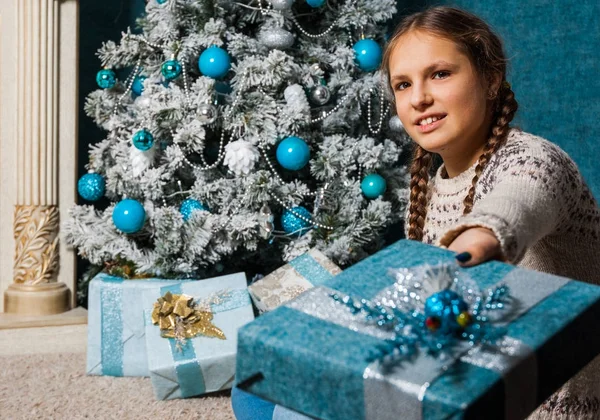 Glückliche Mädchen halten Weihnachtsgeschenkbox am Feiertag Morgen in schönen Raum Interieur. Ein weibliches Kind hält neben geschmücktem Tannenbaum und Kamin ein Weihnachtsgeschenk in den Händen. Winterferienkonzept — Stockfoto