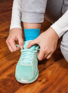 Eller yeşil spor ayakkabı bağlama genç bir kadın. bir ahşap zemin arka planı