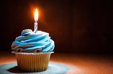 Buttercream ve ahşap masa kopya alanı ile koyu arka plan üzerinde yanan mum ile lezzetli kek.