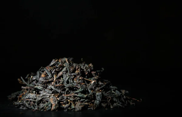 Heap of black tea leaves on the old dark wooden background with copy space