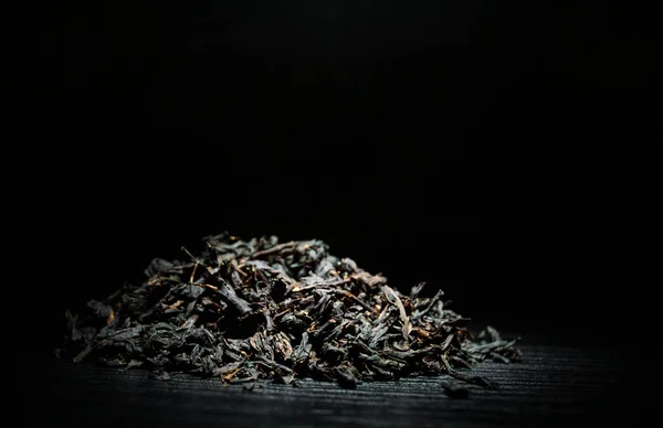 Heap of black tea leaves on the old dark wooden background with copy space