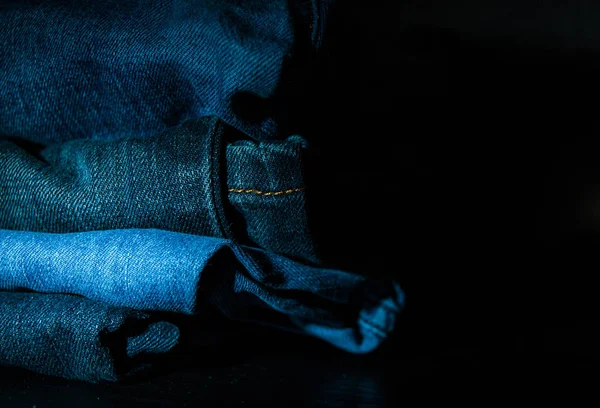 Stack of folded clothes, blue jeans pants, dark blue denim trousers on dark background with copy space.